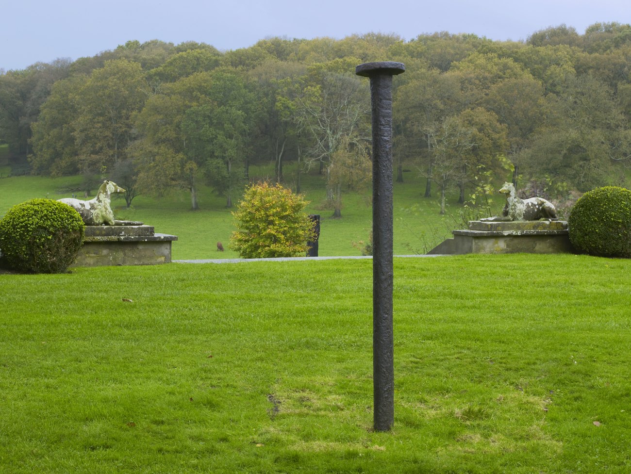 A large black sculpture of a nail stood upright in a grassy garden