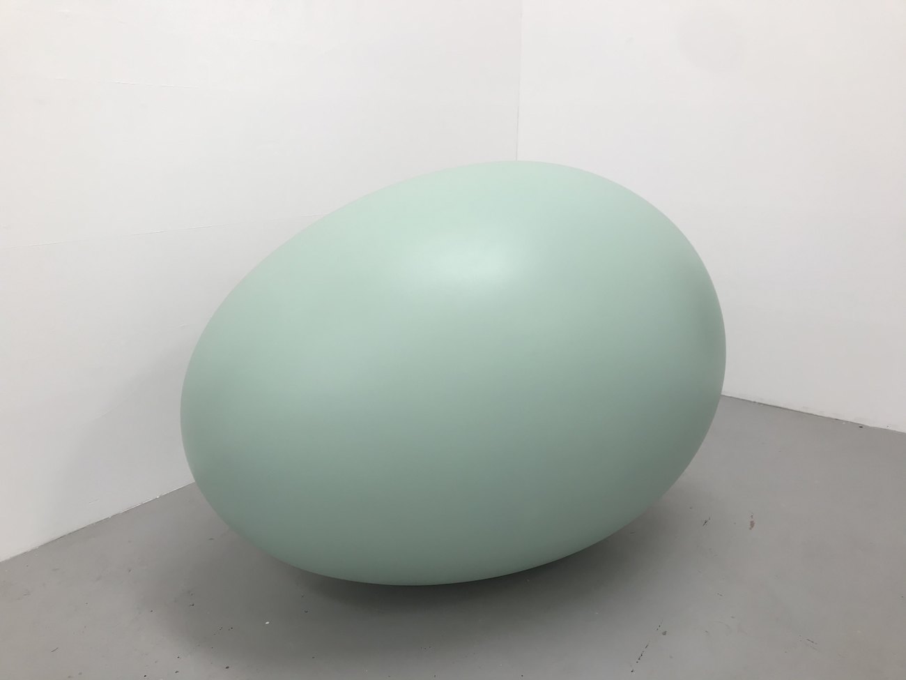 A large turquoise egg sculpture in the corner of a room