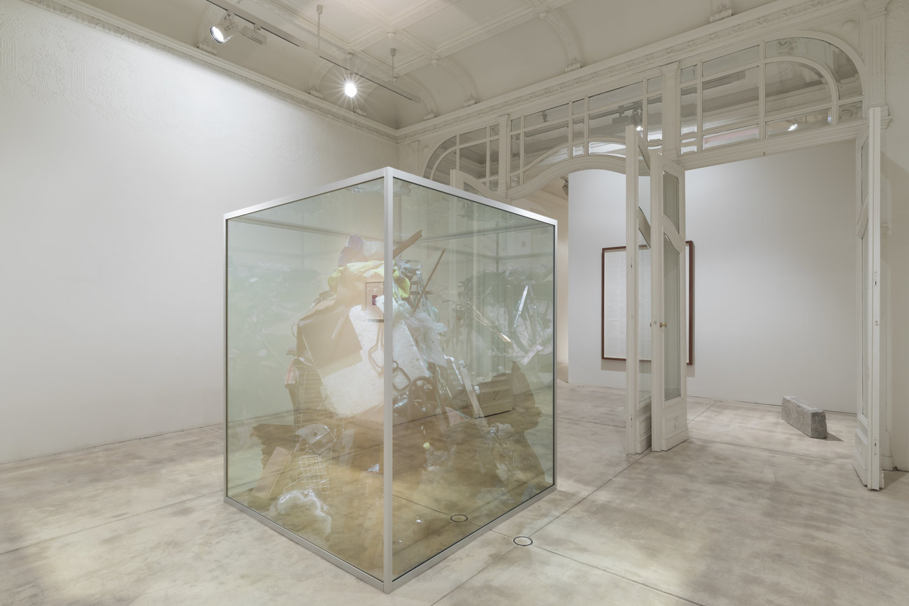 A large glass display case filled with trash in the centre of a white room