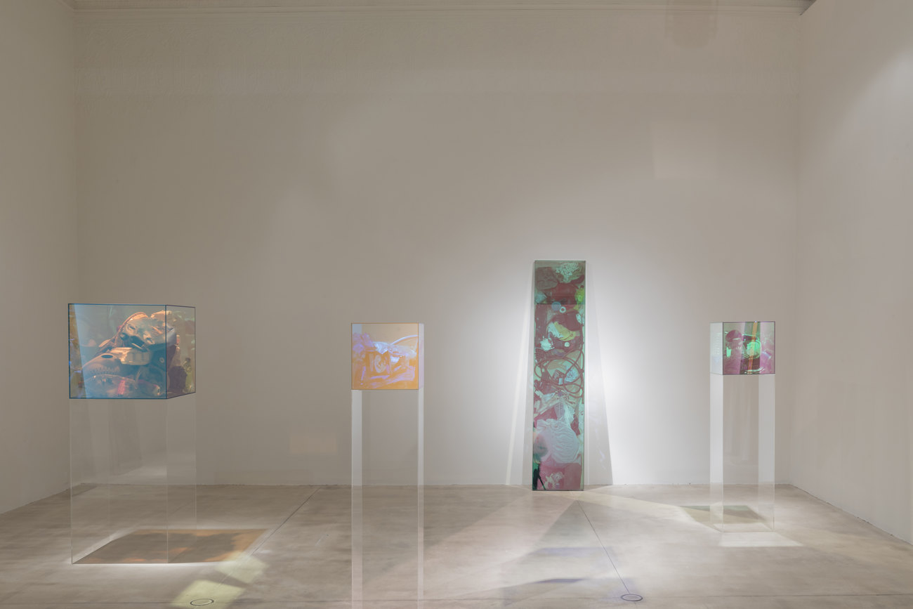 4 glass displays filled with trash and illuminated by coloured lighting in a white room