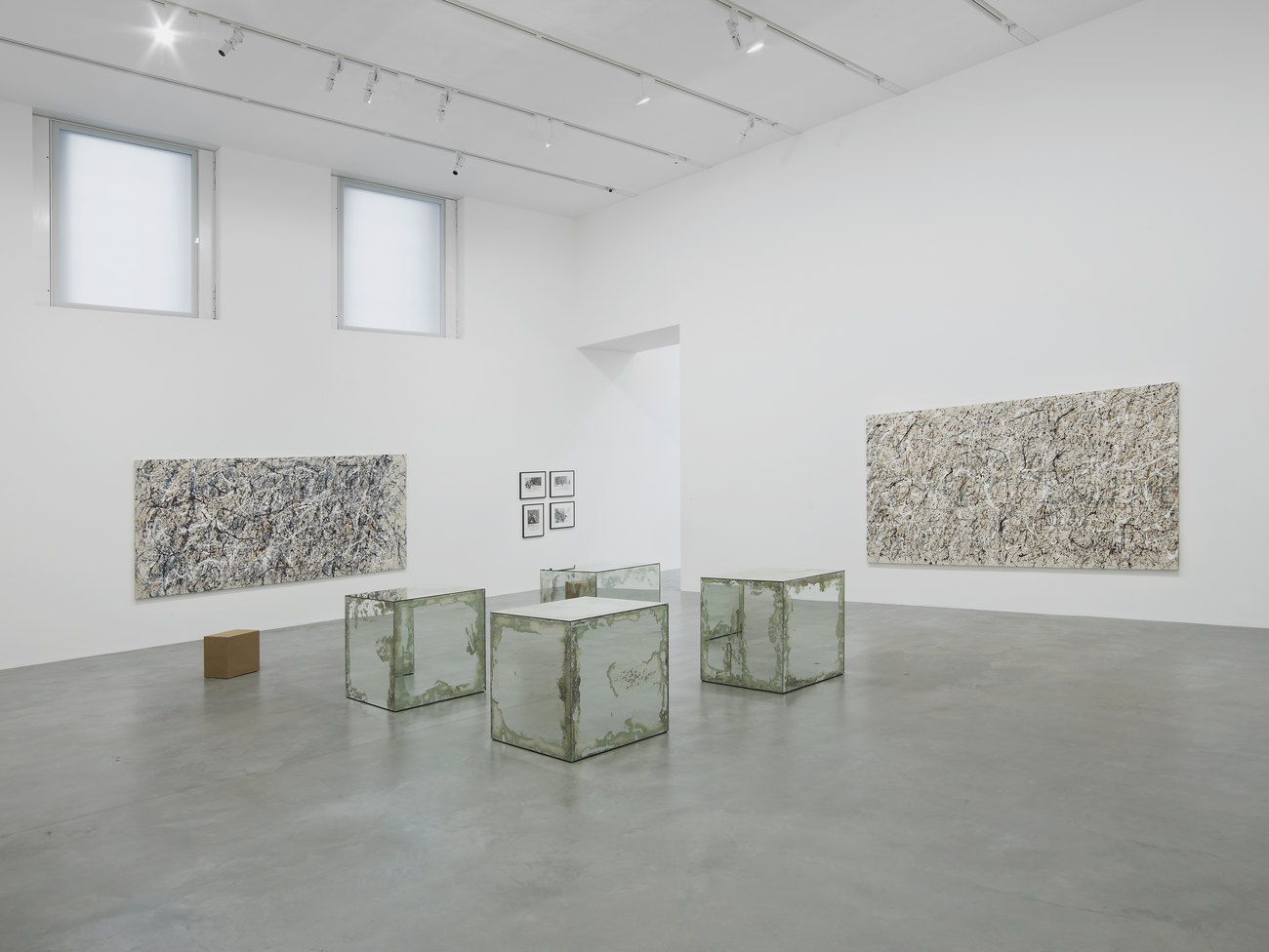 4 mirrored cubes sit in the centre of a room equidistant apart, on the two walls behind are two large paintings