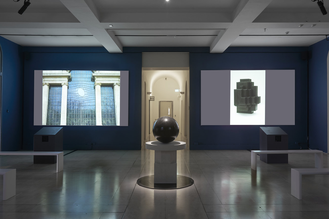 Installation photo of an exhibition incorporating projections of photos of artist's portraits of an egg, and Gavin Turk's sculpture Oeuvre (Black Umber) 