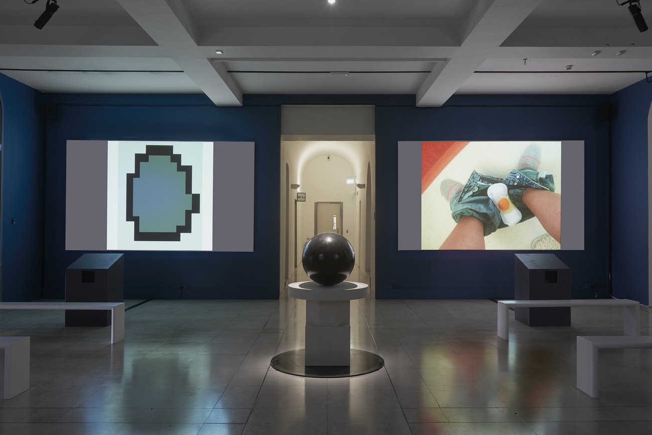 Installation photo of an exhibition incorporating projections of photos of artist's portraits of an egg, and Gavin Turk's sculpture Oeuvre (Black Umber) 