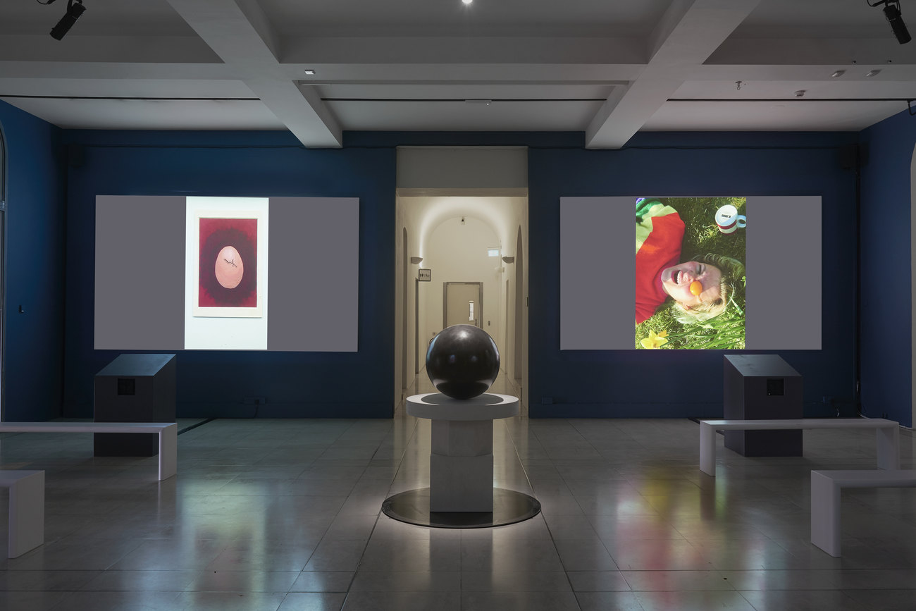 Installation photo of an exhibition incorporating projections of photos of artist's portraits of an egg, and Gavin Turk's sculpture Oeuvre (Black Umber) 
