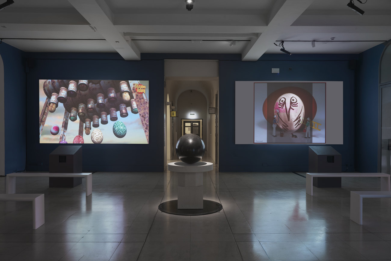 Installation photo of an exhibition incorporating projections of photos of artist's portraits of an egg, and Gavin Turk's sculpture Oeuvre (Black Umber) 