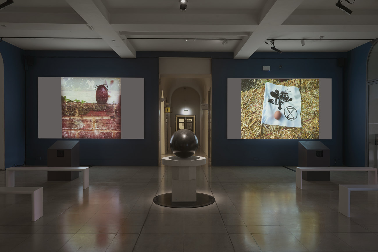 Installation photo of an exhibition incorporating projections of photos of artist's portraits of an egg, and Gavin Turk's sculpture Oeuvre (Black Umber) 