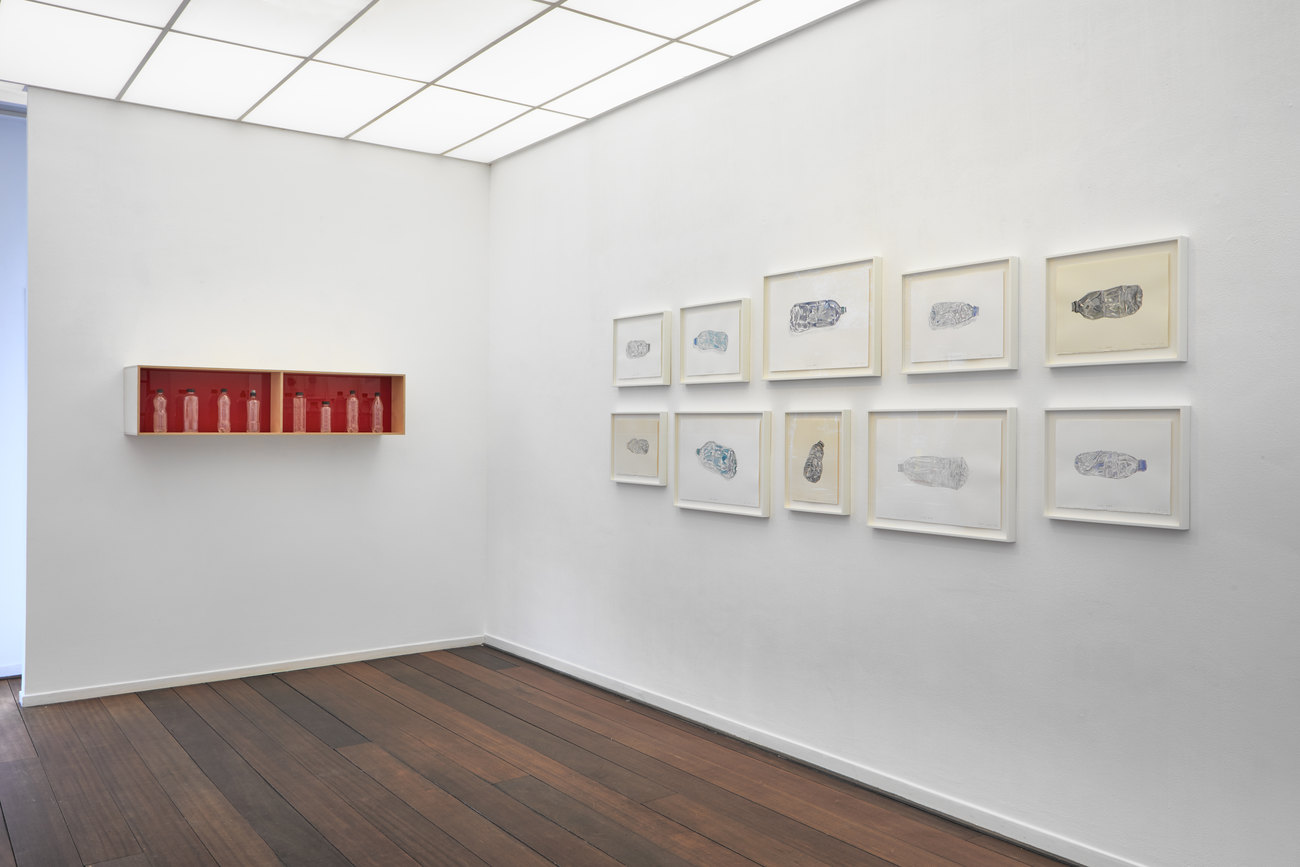 Installation photo of water colours of used/discarded bottles, and a display box with red acrylic inside, displaying used water bottle