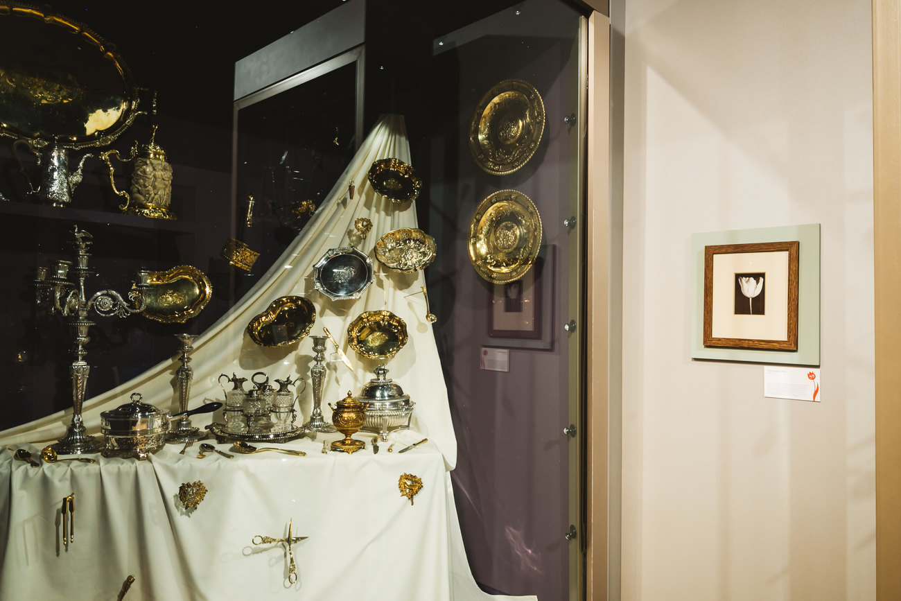 An image shows an installation of silver plates and table cloth, to the right hand side a photograph of a Tulip by Charles Jones 