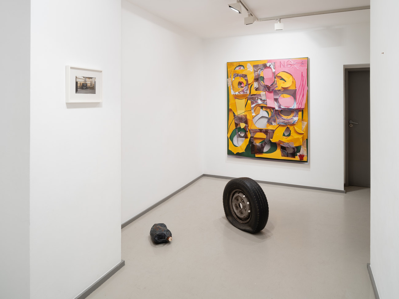 The photo shows a bright painting by Neil Gall in the background and forefront is a bronze cast flat tyre and a bronze cast oil bottle